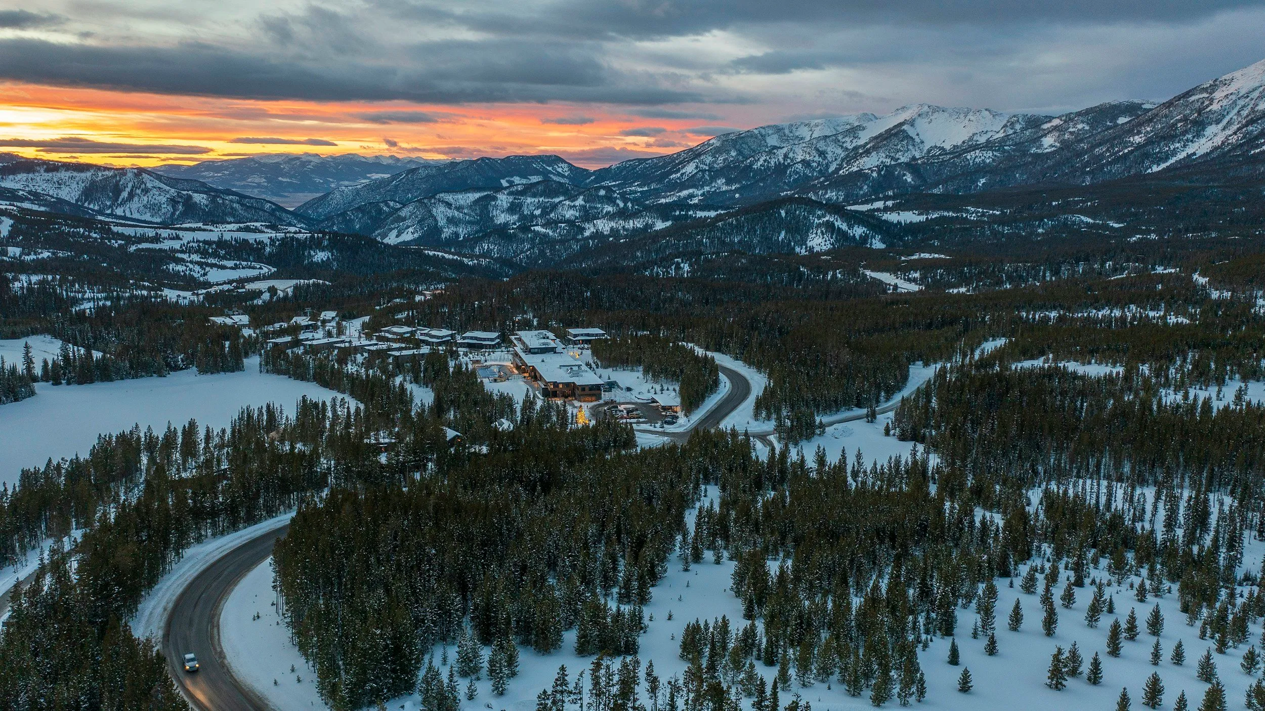 Snow-covered valley and forest below mountain peaks at sunset