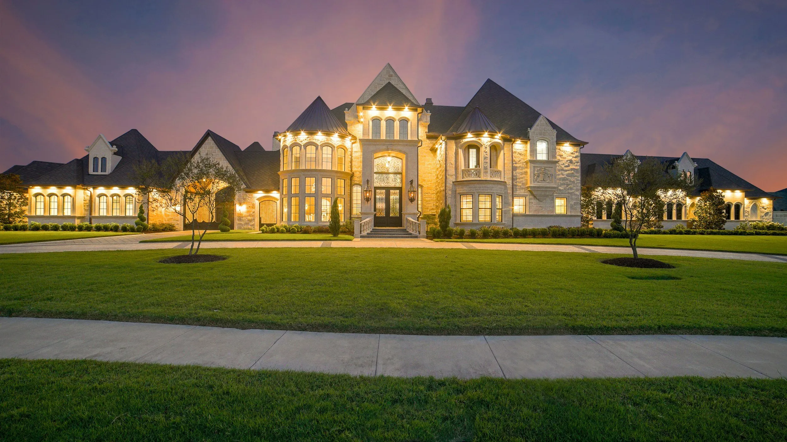 Large stone and stucco house lit up at dusk under a purple sky