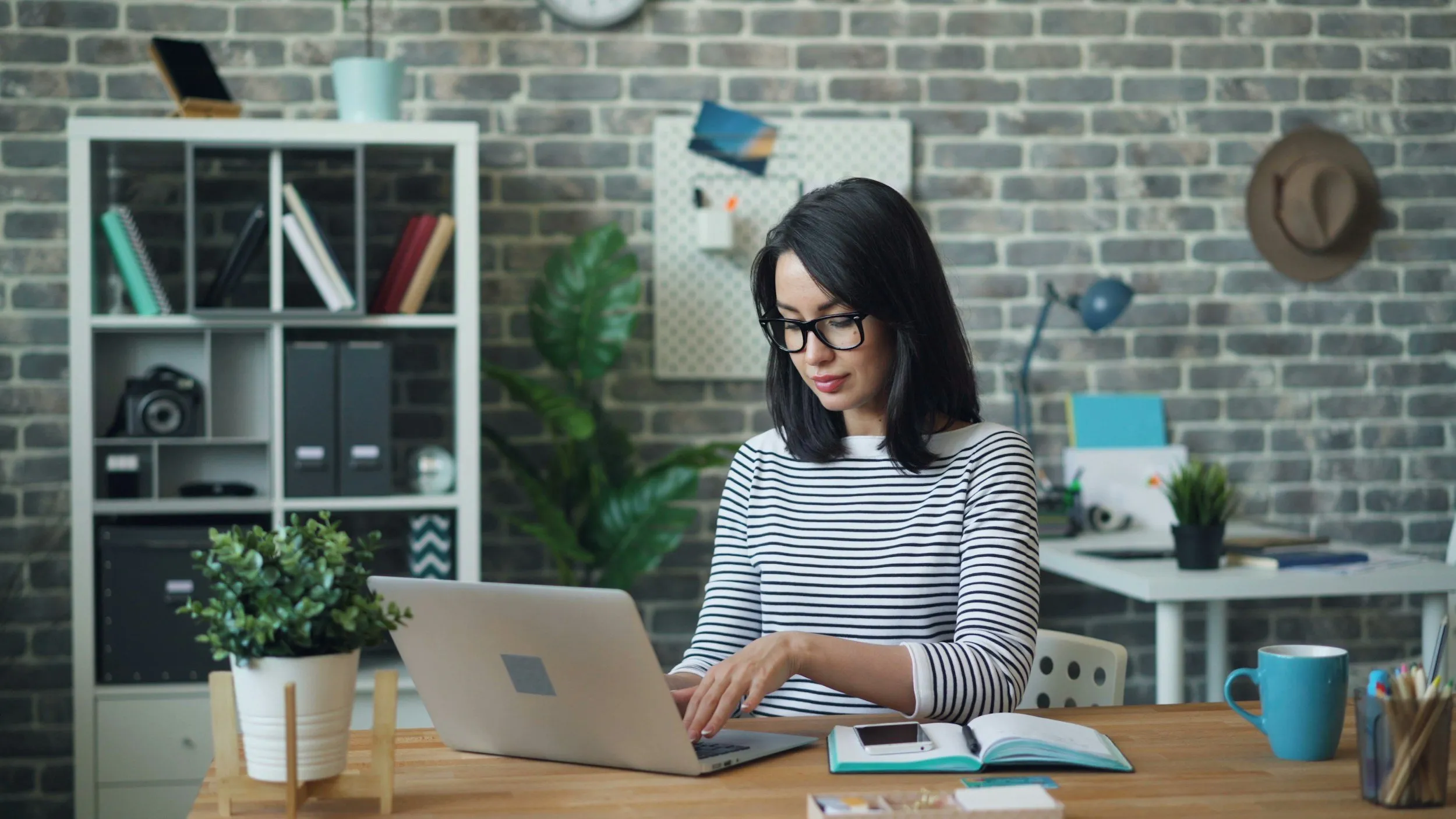 A household manager working at a laptop at a desk with bookshelves and plants